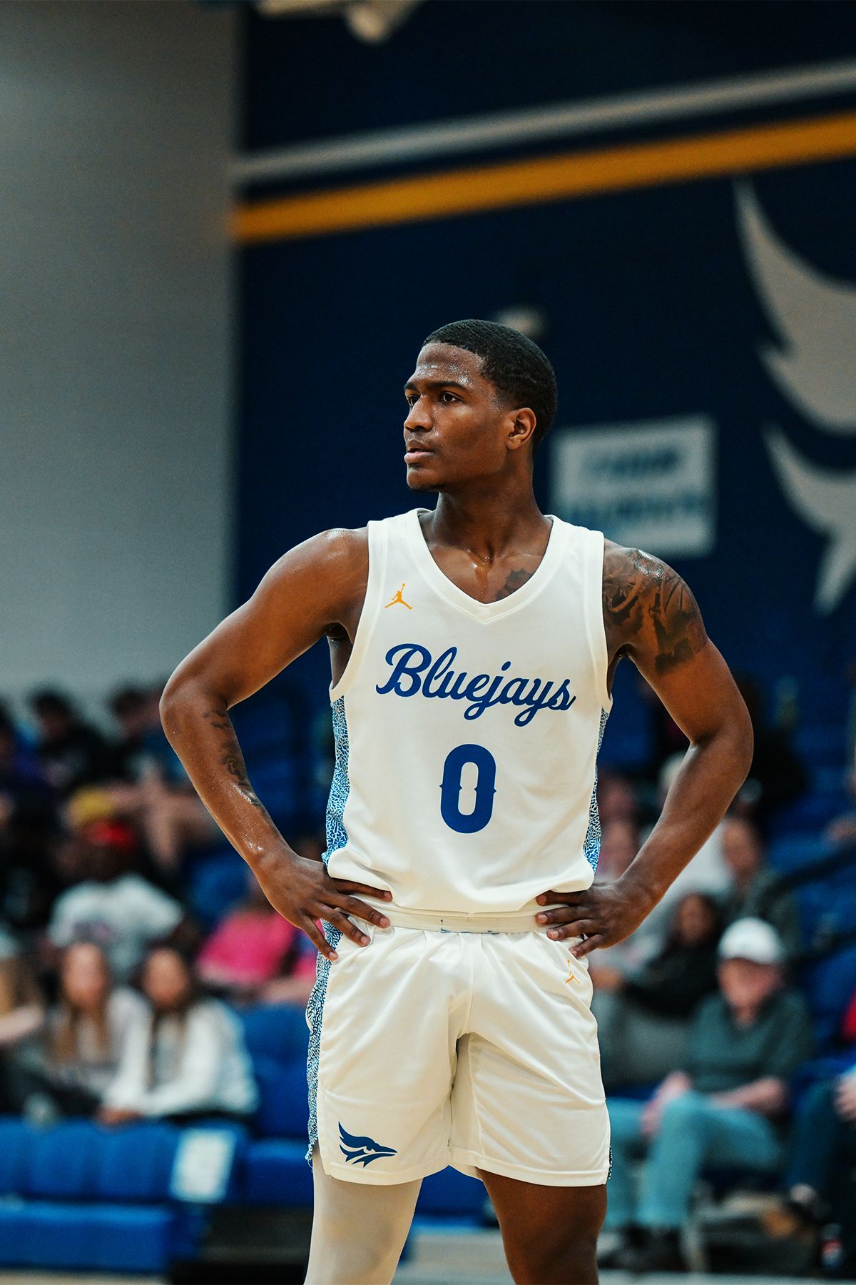 Basketball player in white Bluejays jersey number 0 stands with hands on hips.