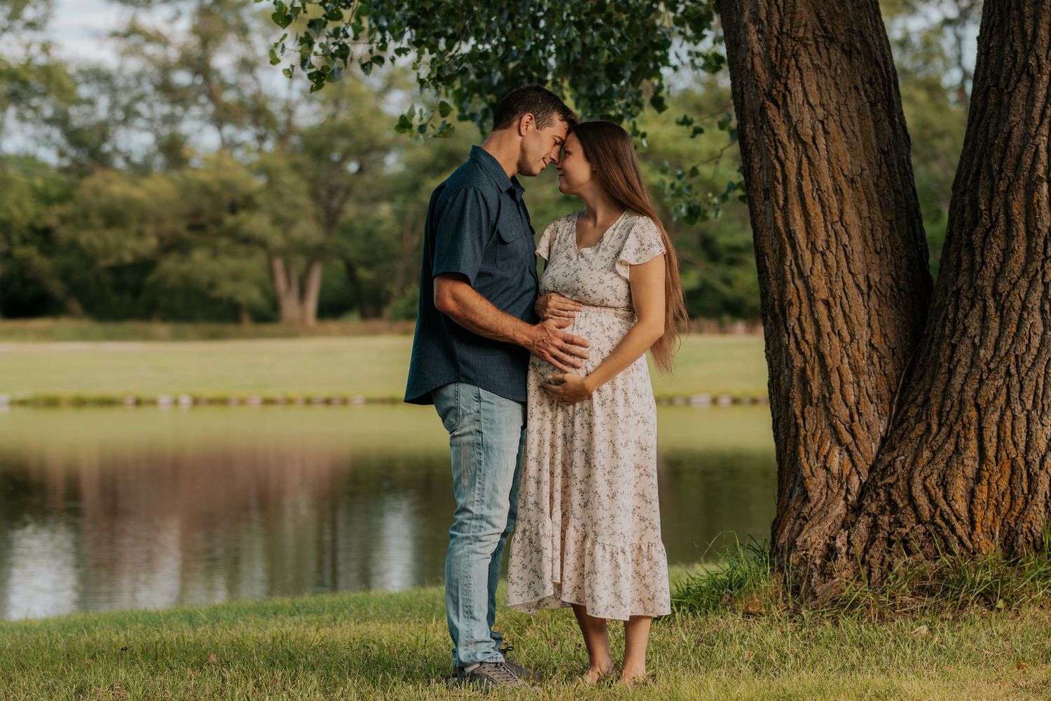 Romantic couple embraces near a lake under tall trees during a sunset photo session in the countryside.