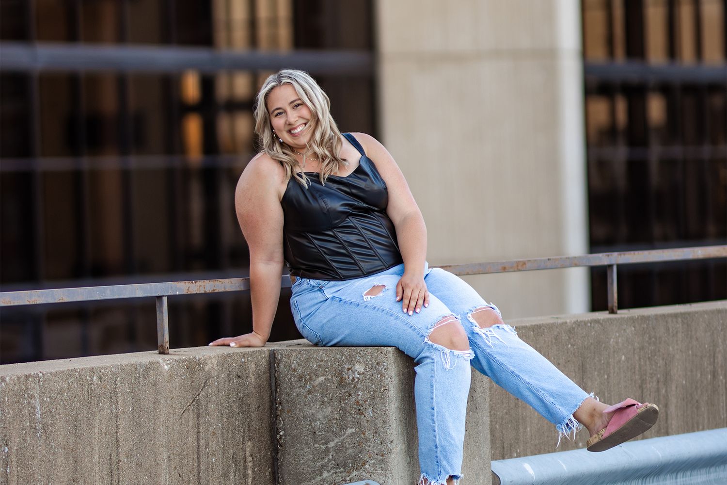 Casual portrait of someone in black tank top and ripped jeans sitting on concrete ledge.