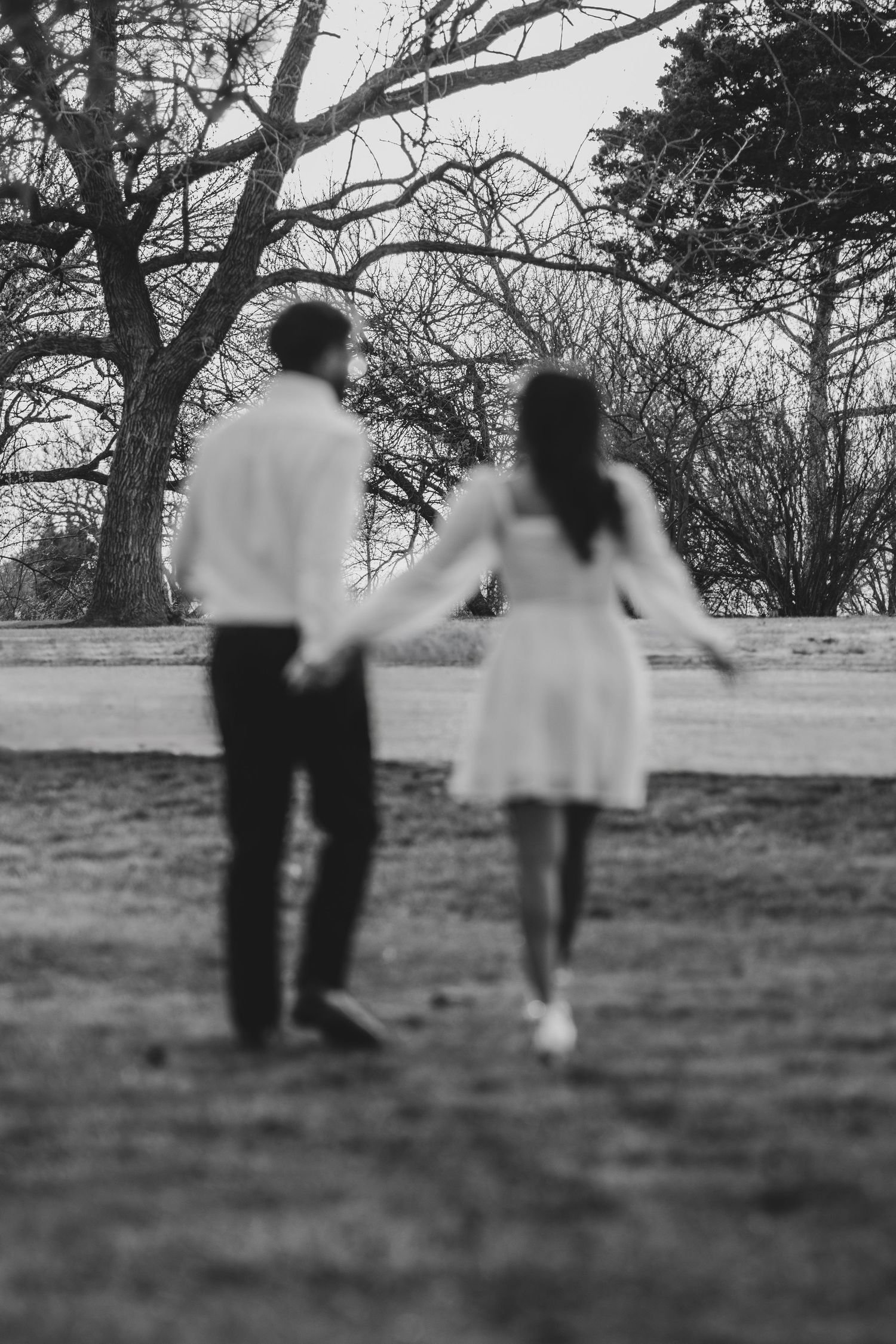 Black and white photo of couple holding hands while walking in park.