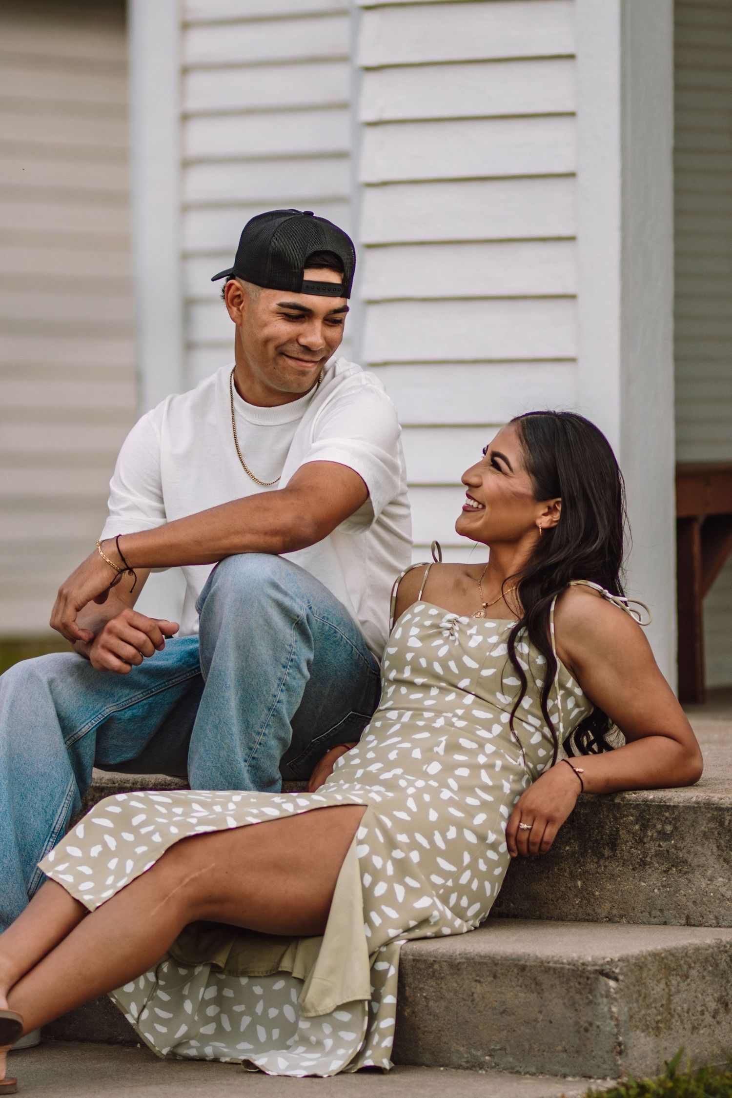 Three sequential images show a couple sitting together and laughing playfully on concrete steps by a white building.
