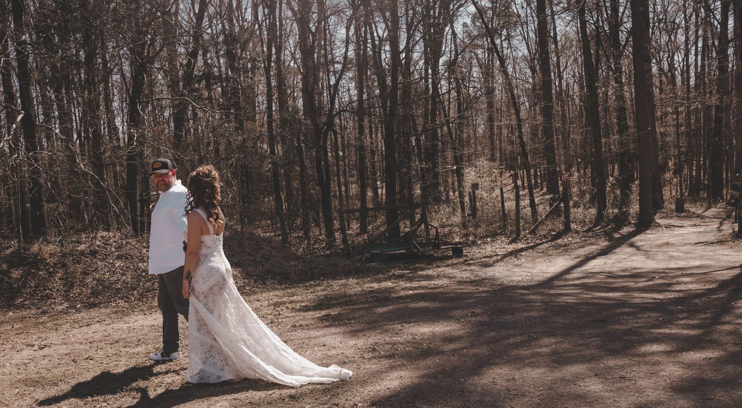 A wedding couple walks hand in hand along a wooded path in elegant attire.