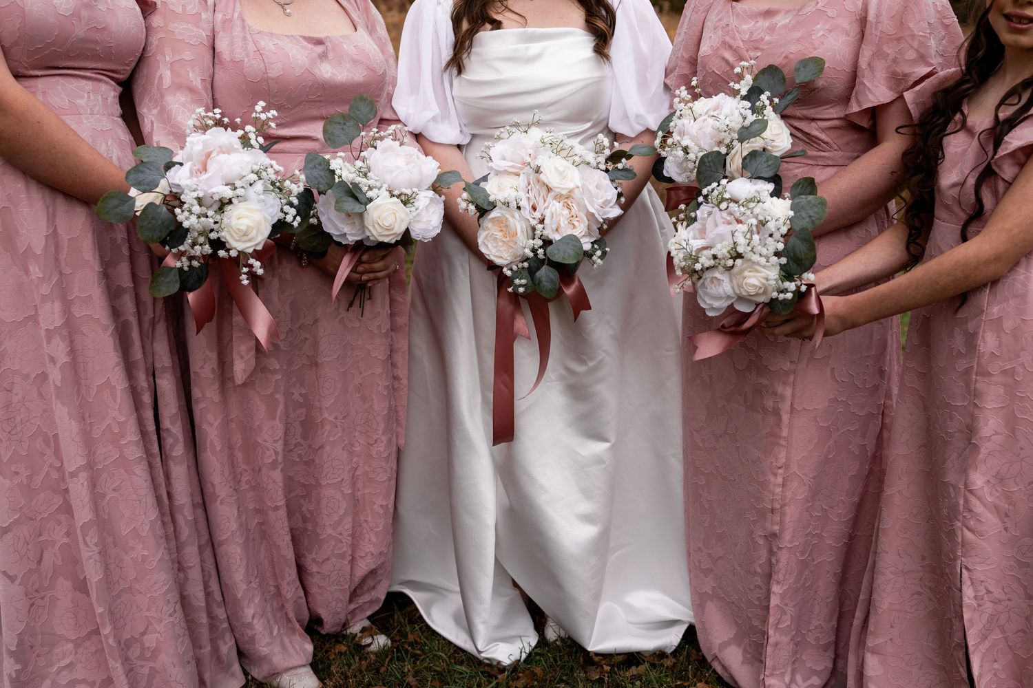 Bride in white gown with bridesmaids in dusty rose dresses holding white and pink floral bouquets.