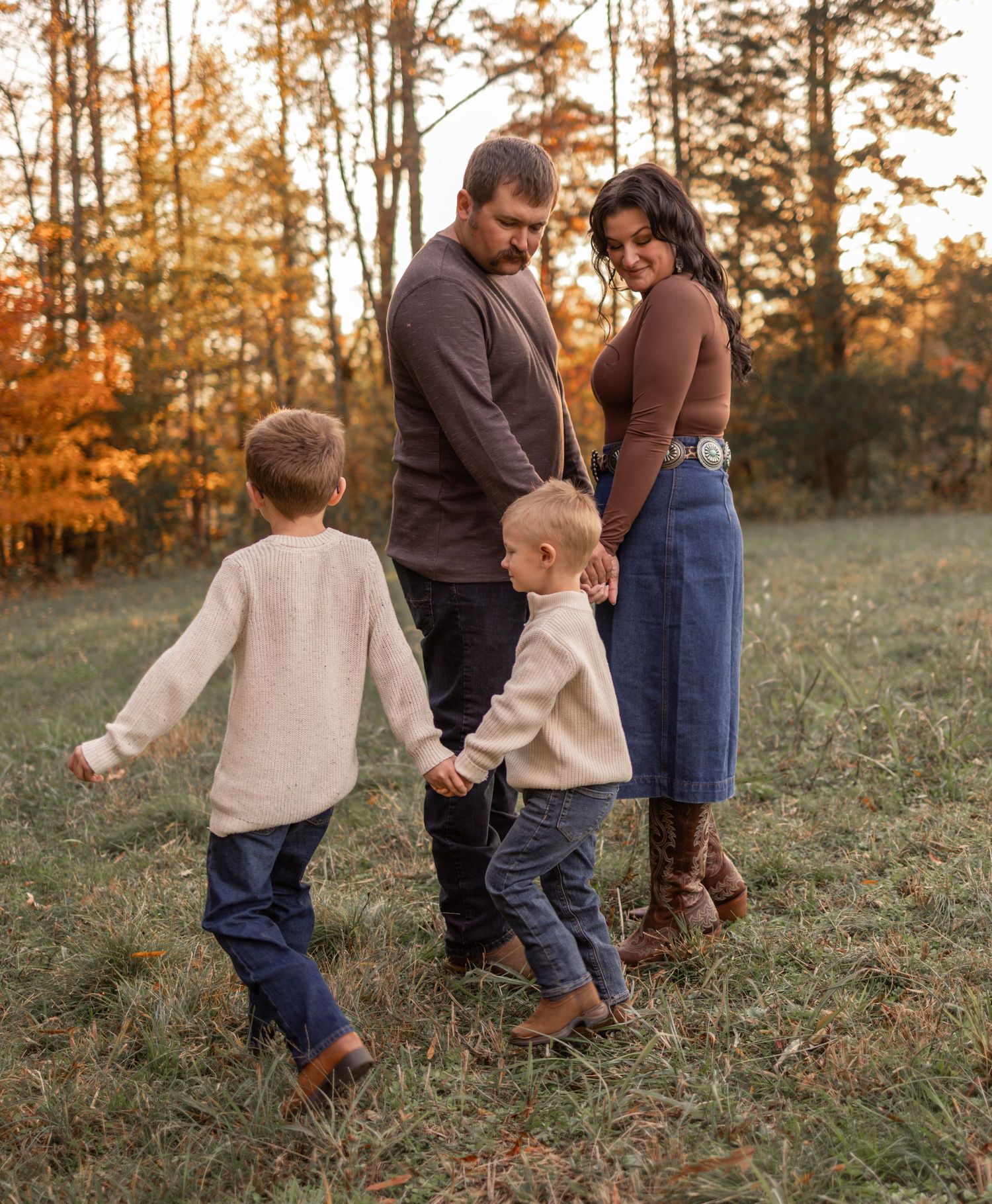 A family walking together in a grassy field during golden hour sunset in autumn.