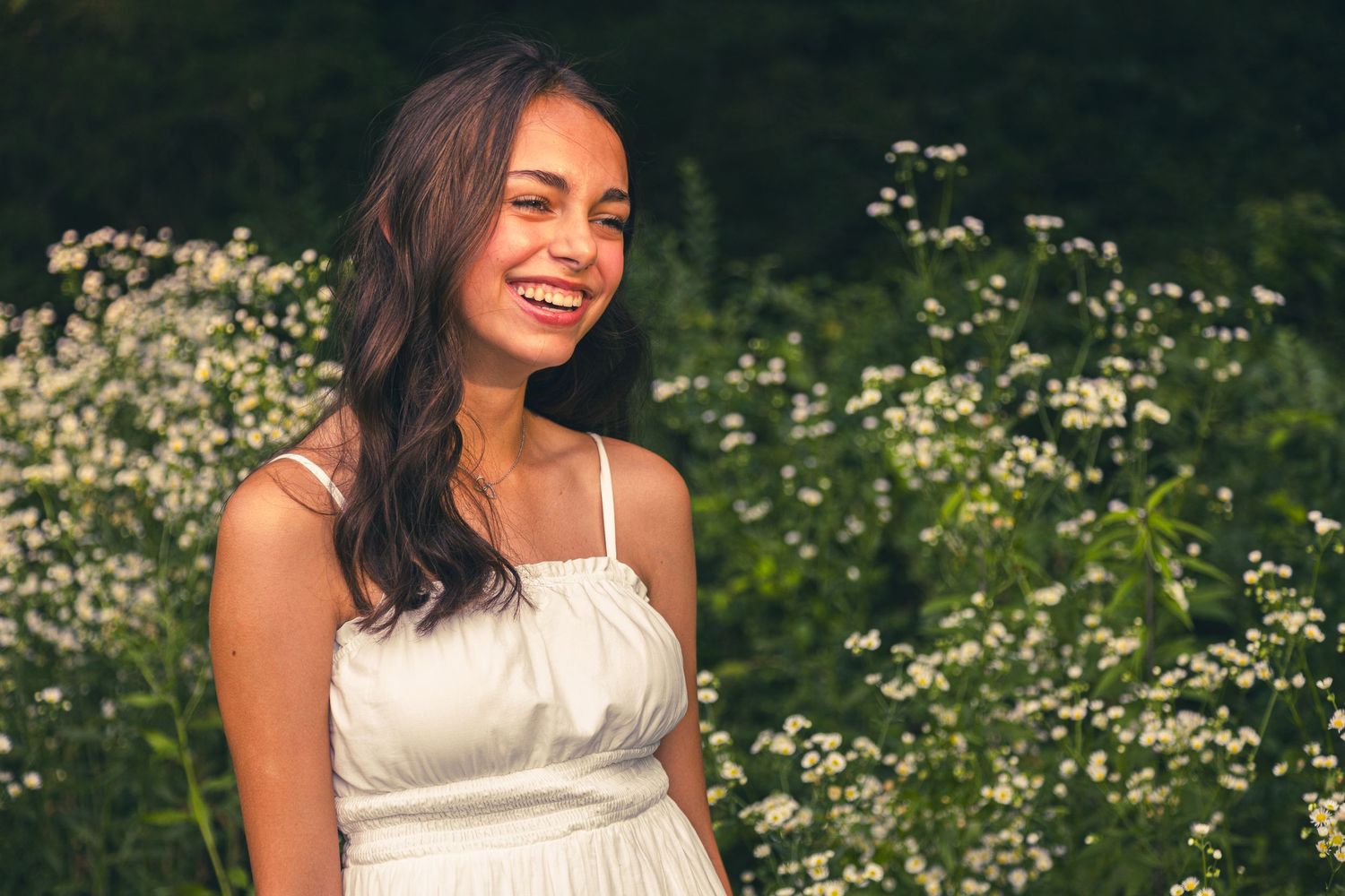Summer portrait in a white dress surrounded by wildflowers and greenery.