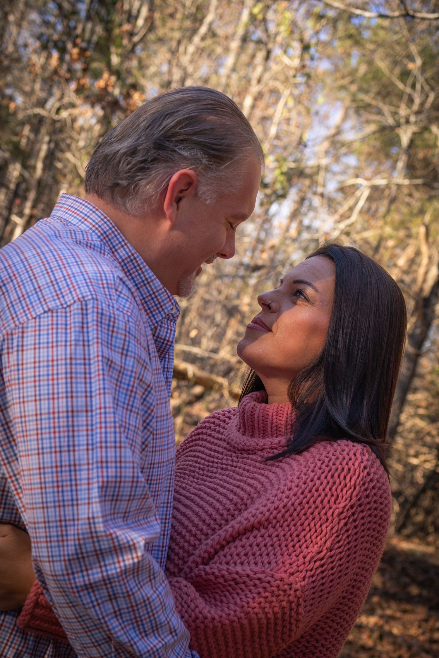 A couple shares a tender embrace outdoors in an autumn forest setting.