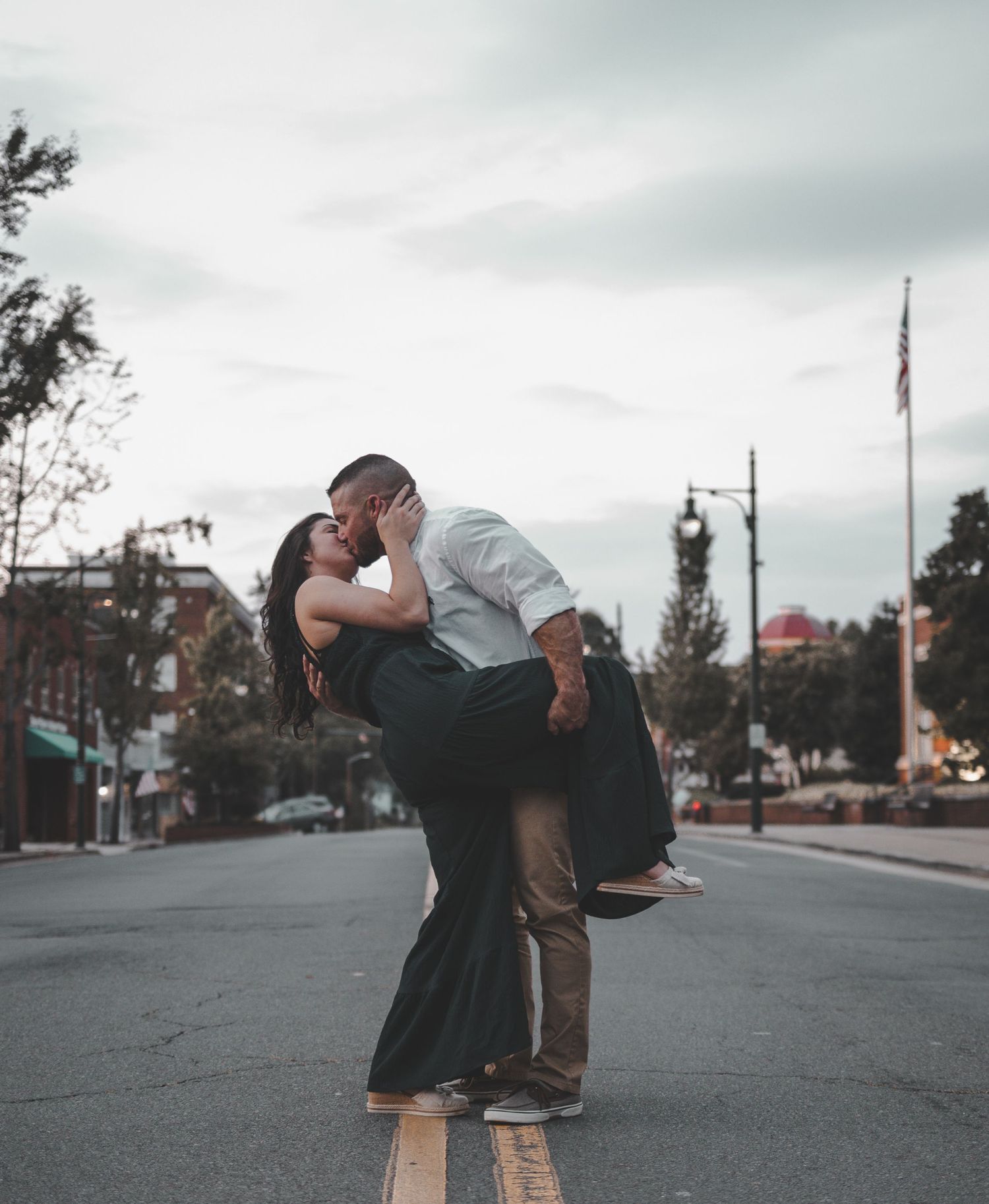 Couple sharing romantic kiss on empty street with moody sky backdrop.