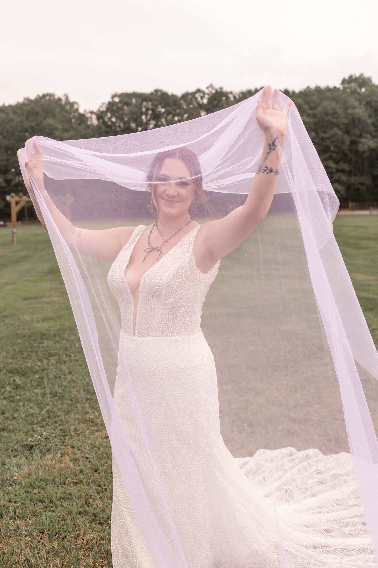 A bride in a white dress playfully twirls with her veil in a grassy outdoor setting during a golden hour photoshoot.