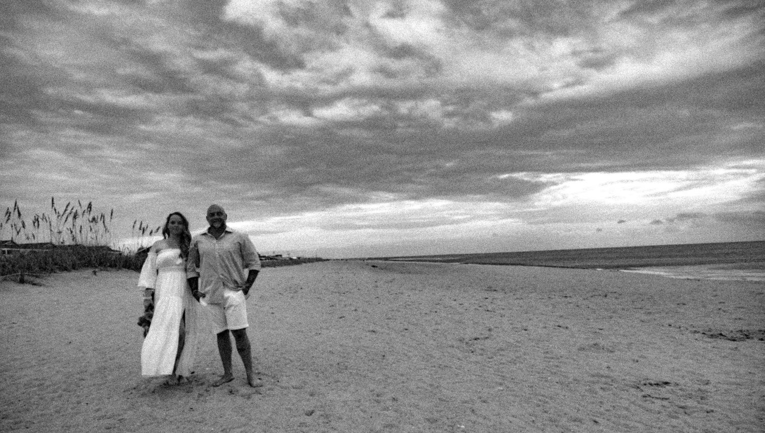 Monochrome seaside sequence shows people walking along a beach with dramatic cloudy skies above.