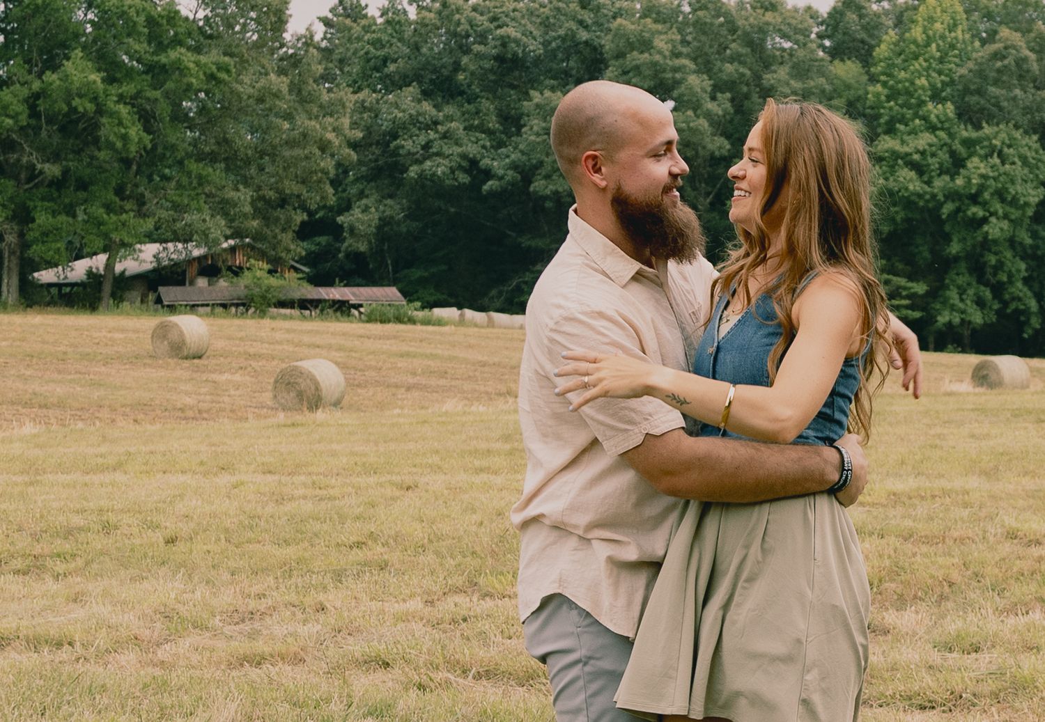 Romantic embrace in a golden field with round hay bales in the background.
