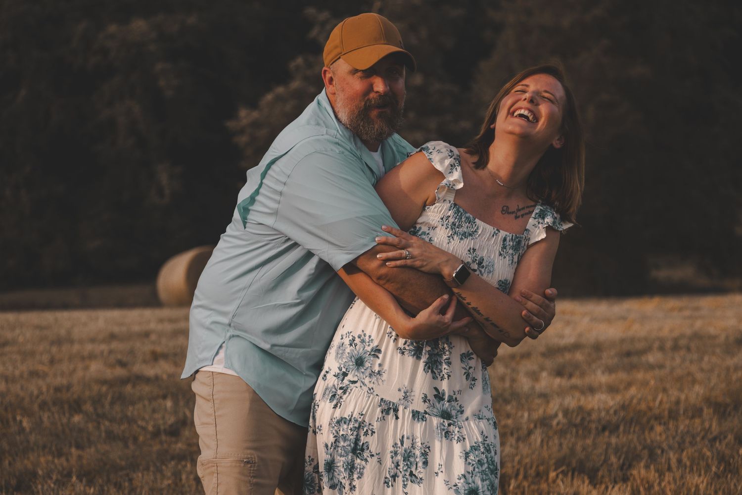 A joyful couple embraces and laughs together in a golden field at sunset.