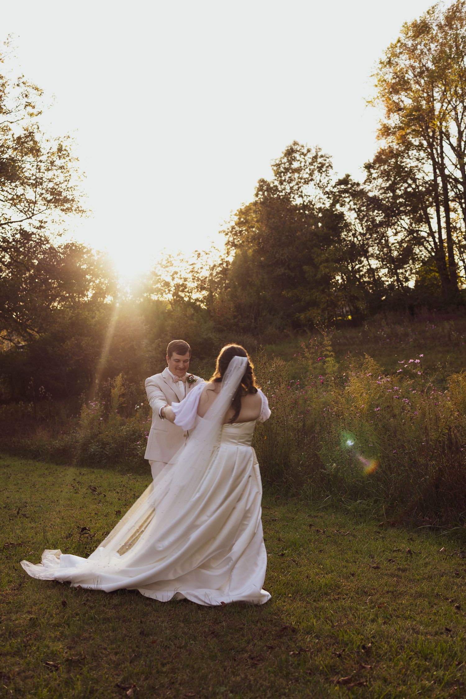 Bride and groom share a romantic dance outdoors at golden hour, surrounded by lush green trees and warm sunlight.