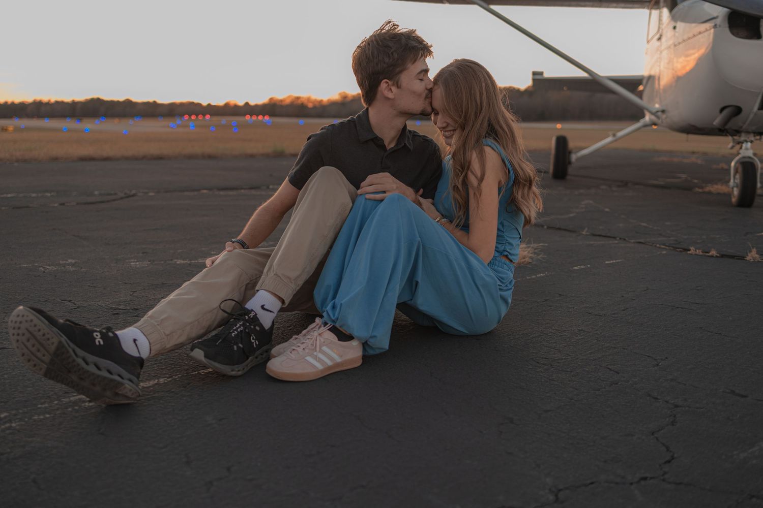 A couple sits together on the ground at sunset sharing an intimate moment on a dark surface.