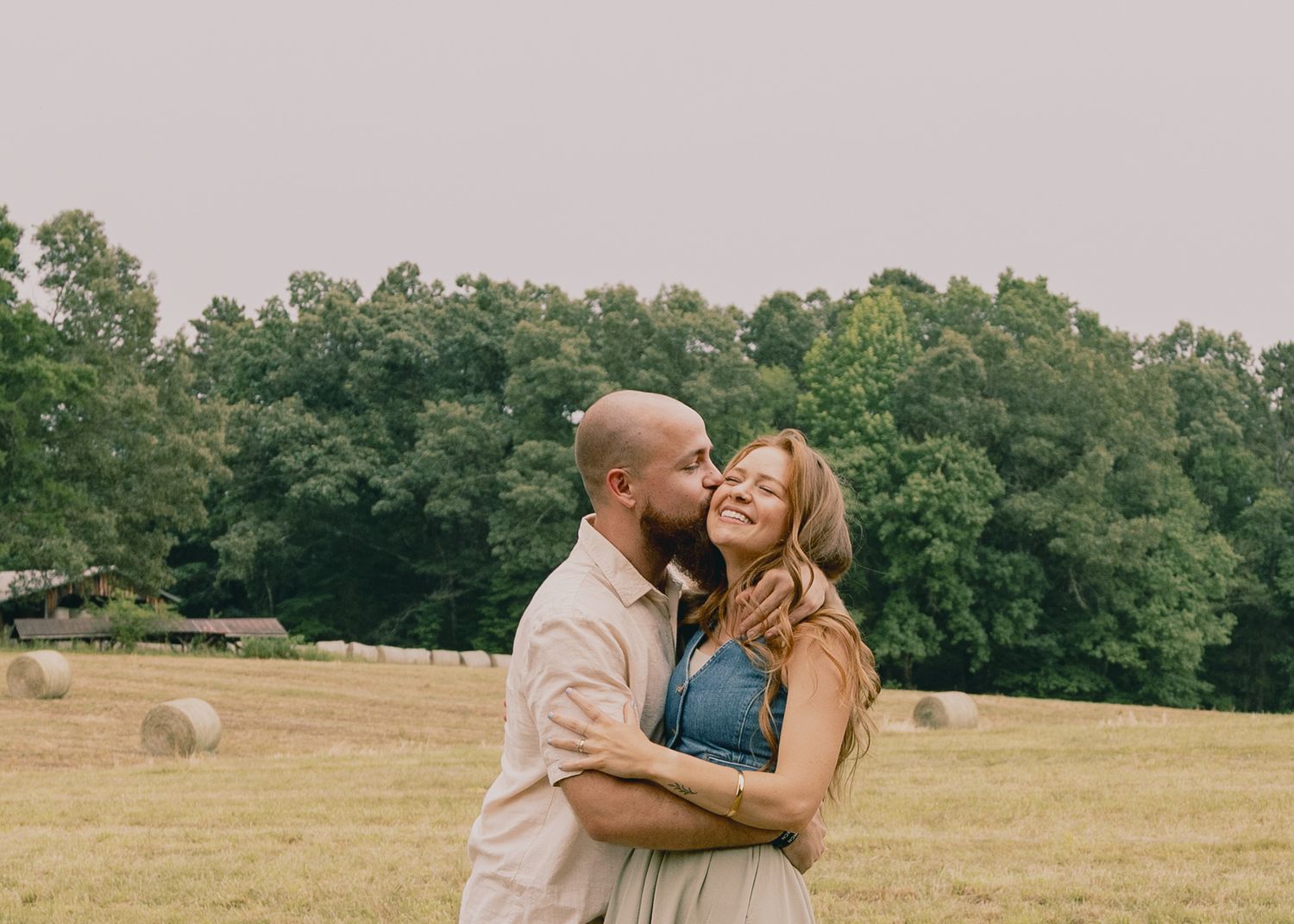 Joyful couple sharing laughter while embracing in a rustic field setting.