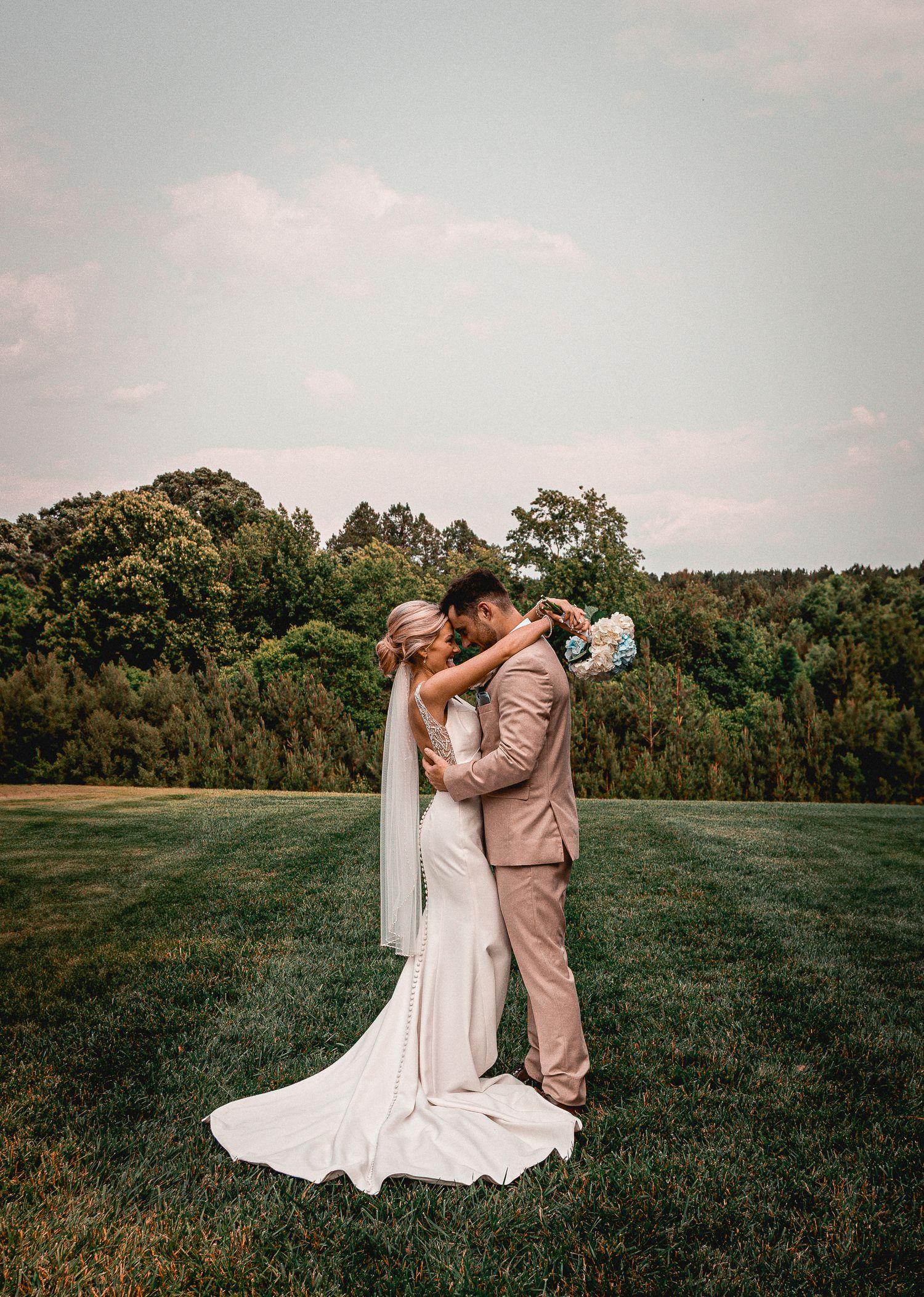 Romantic wedding couple dancing together on expansive green lawn.