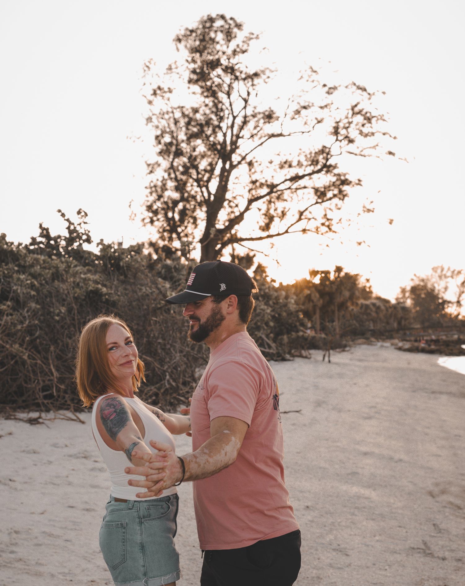 A couple shares a joyful embrace while standing on a dirt path at sunset with trees in the background.