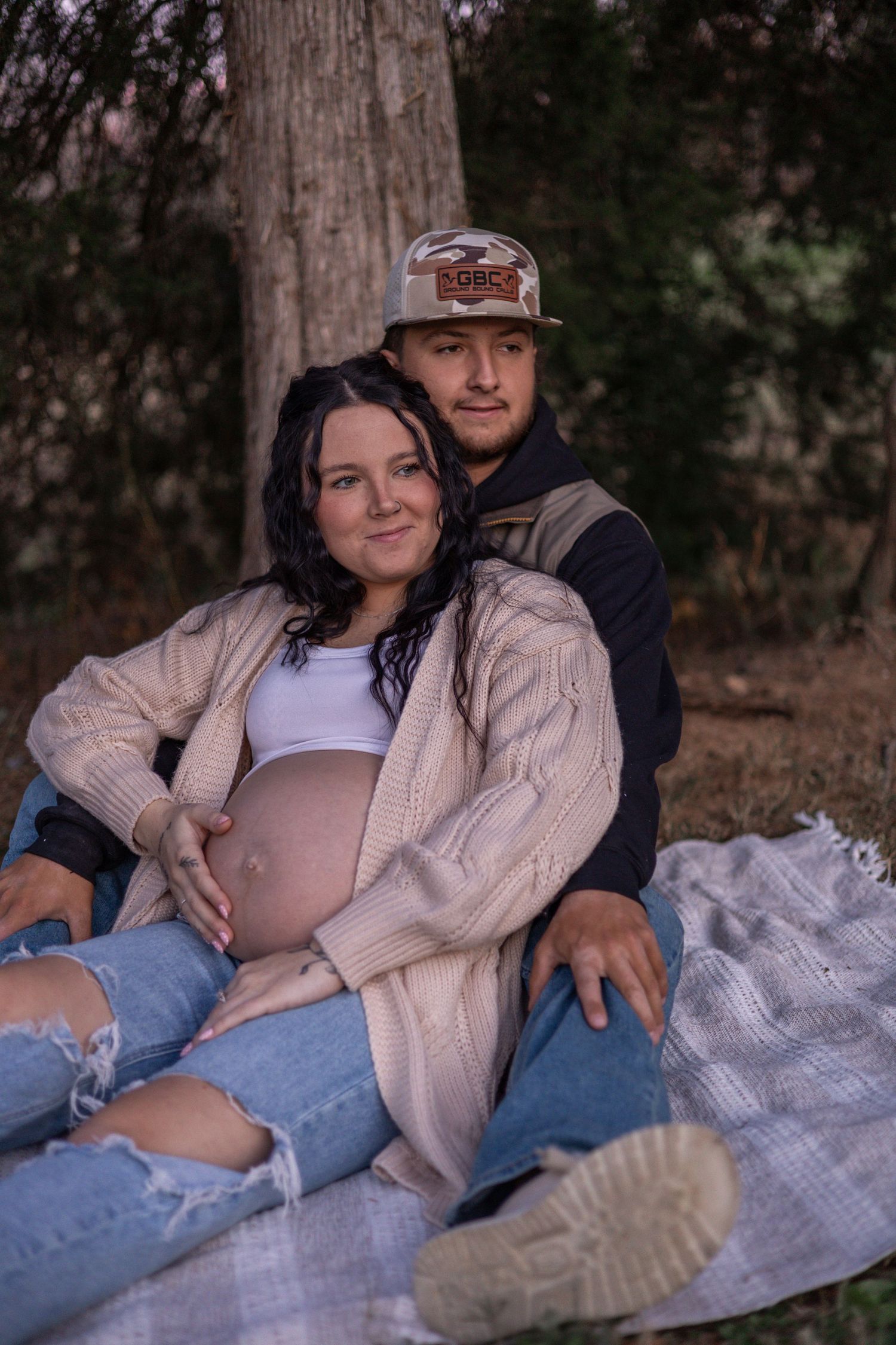 A couple sits together on a blanket outdoors sharing intimate moments in a series of romantic maternity photos.