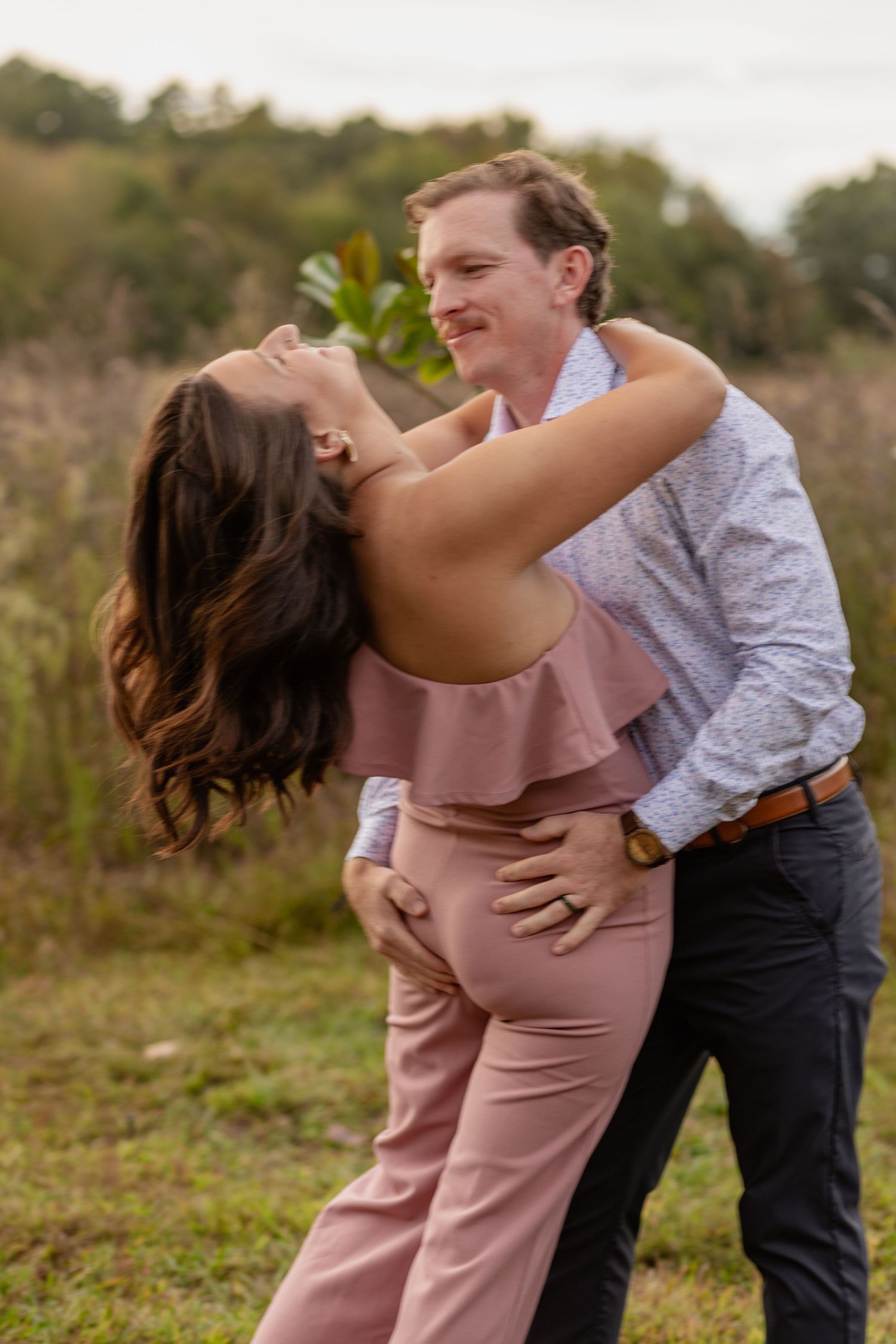 A couple shares a playful moment dancing together in a sunlit meadow.