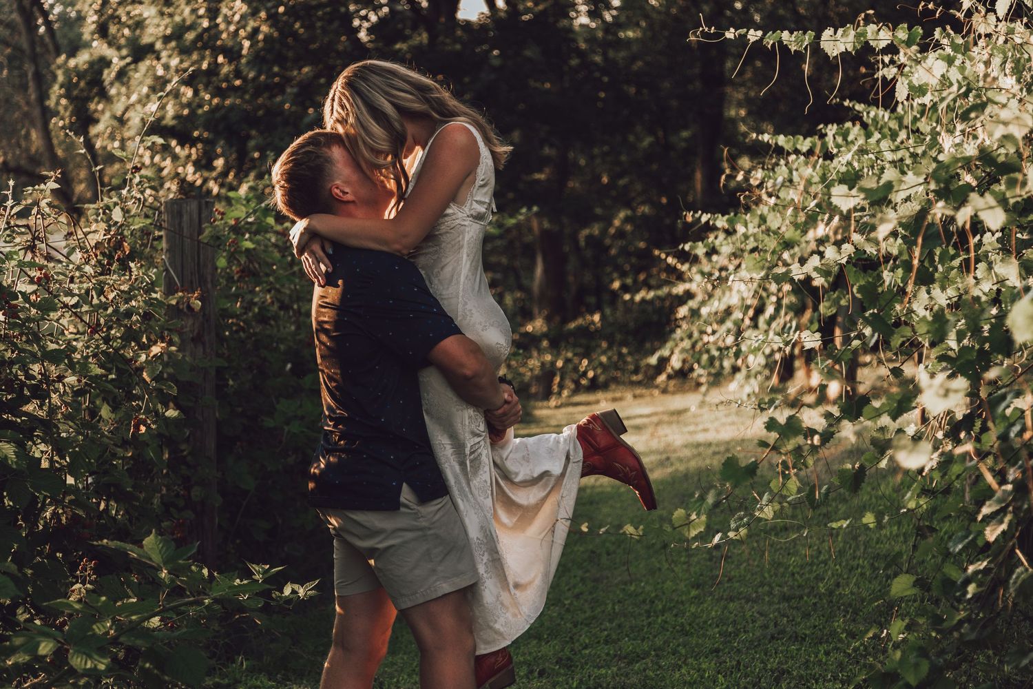 Couple embracing in garden setting with romantic sunset lighting.