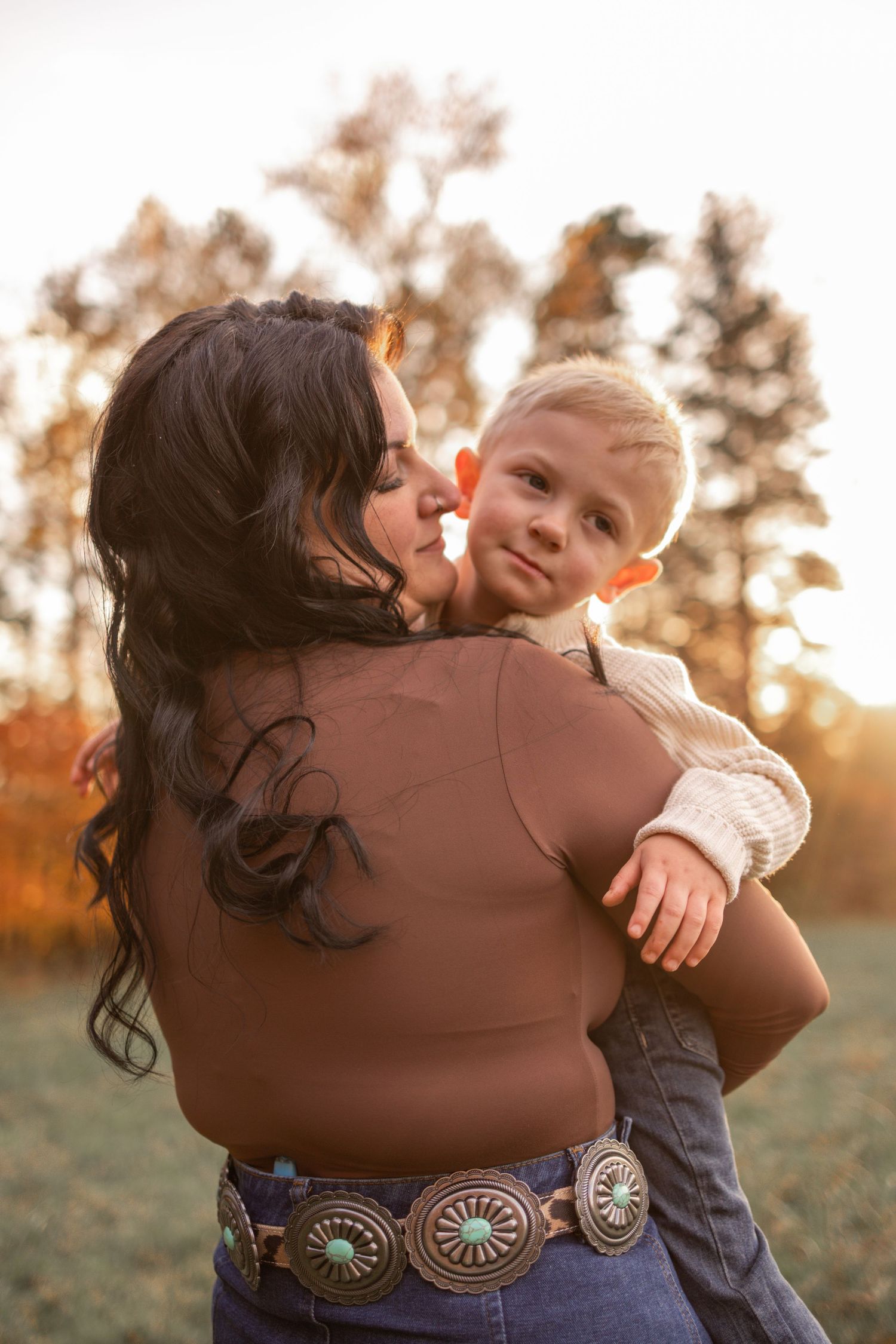 A tender moment between parent and child captured in a series of warm sunset photos in a grassy field.