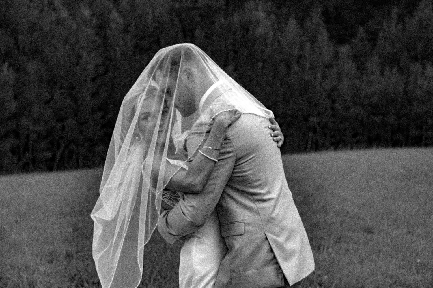 A black and white wedding portrait showing an intimate moment shared under a flowing veil.