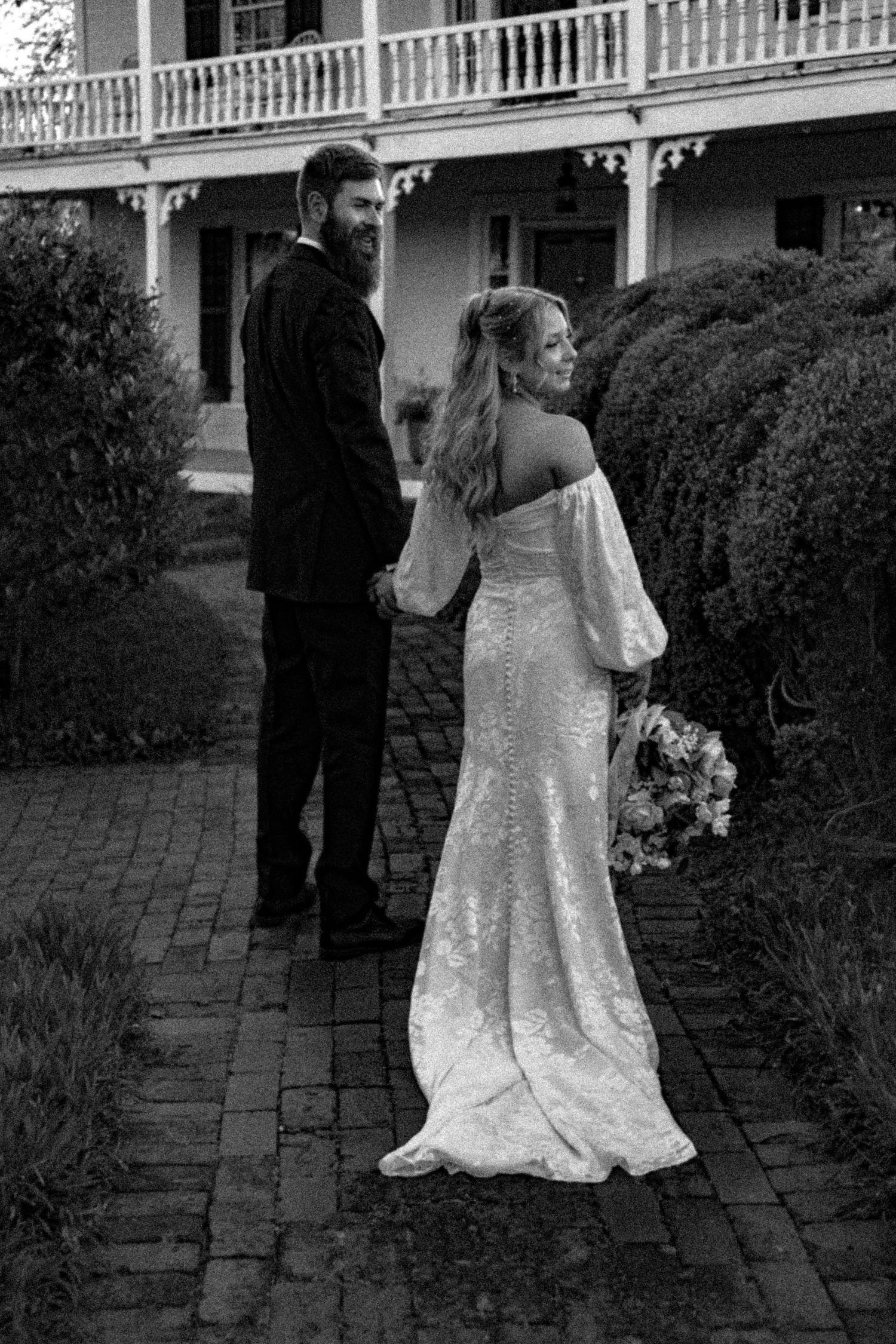 Romantic couple walks along brick pathway outside historic southern mansion.