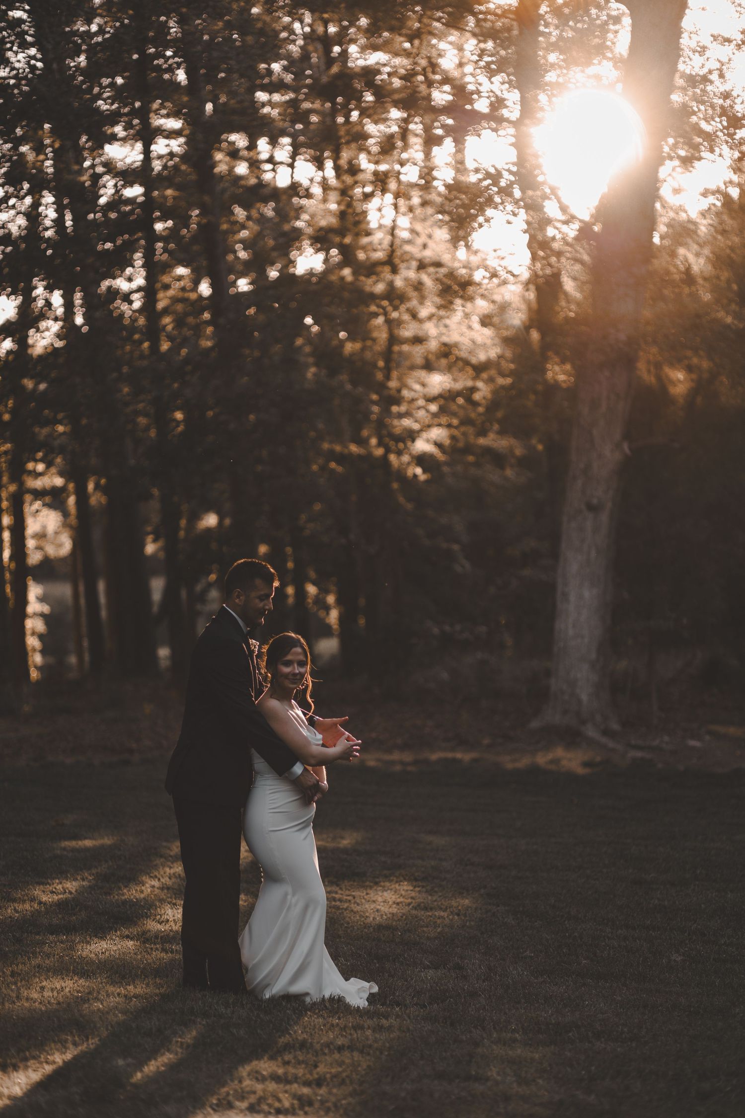 A tender wedding moment captured during golden hour with forest sunlight streaming through the trees.