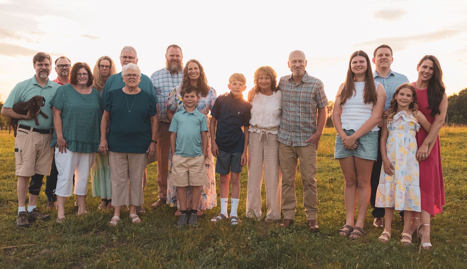 Large multigenerational family posing together outdoors at golden hour in a green field.