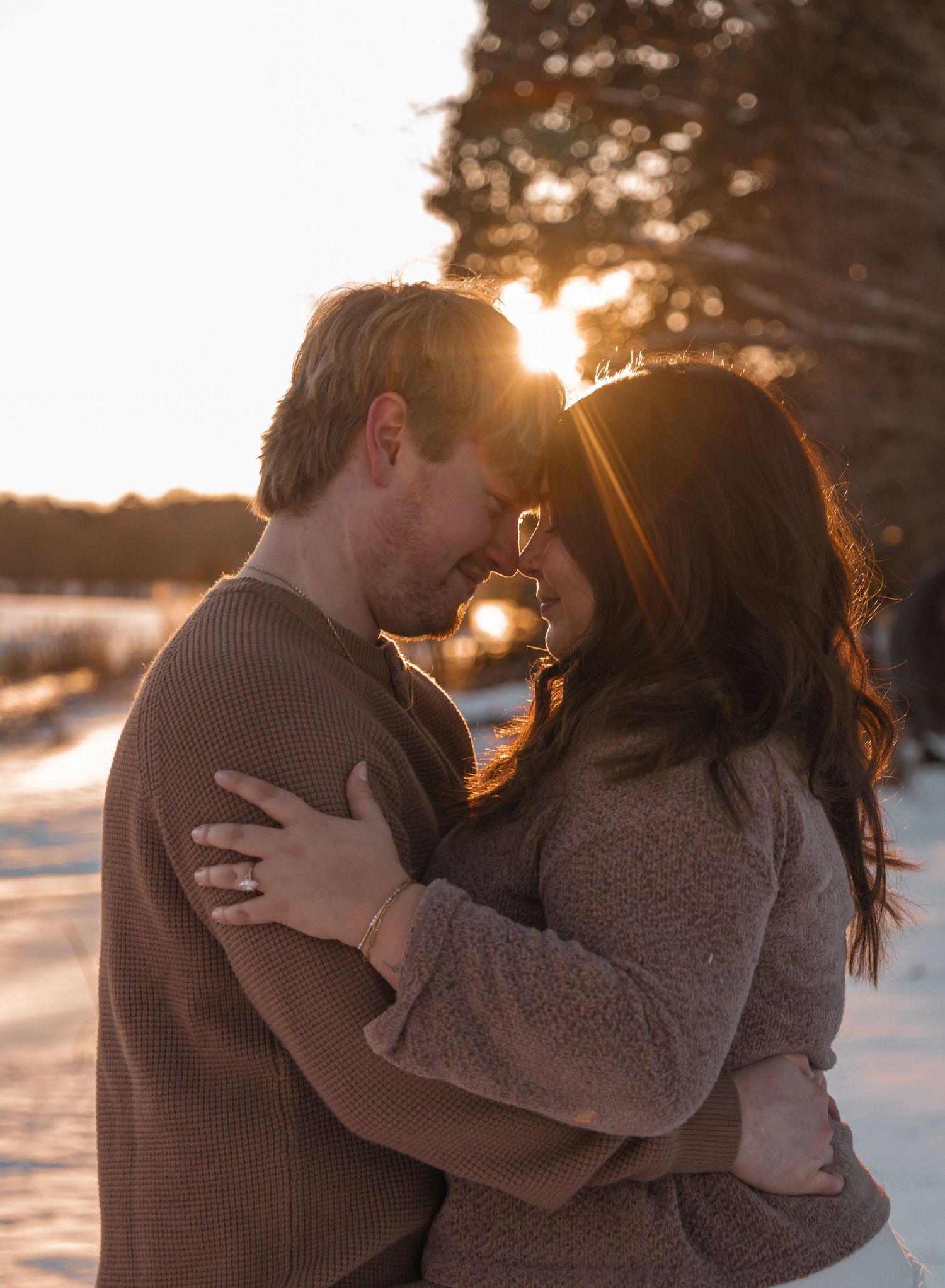 Couple embracing and sharing a romantic moment at golden hour in a snowy winter landscape.