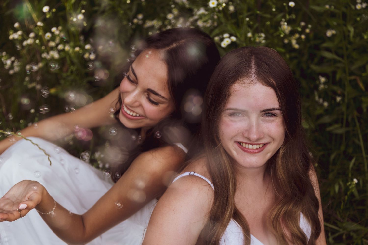 Friends in white dresses sharing joyful moments among blooming flowers.