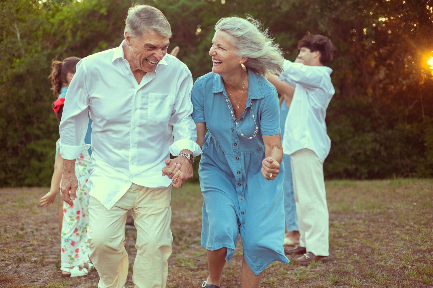 Happy elderly couple holding hands and walking outdoors in a sunny park, smiling joyfully together.
