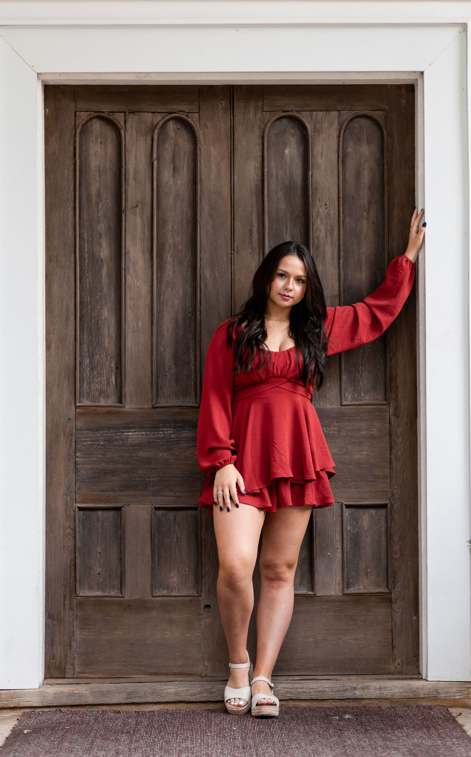 Woman in red dress poses against dark wooden door in artistic fashion photo series.