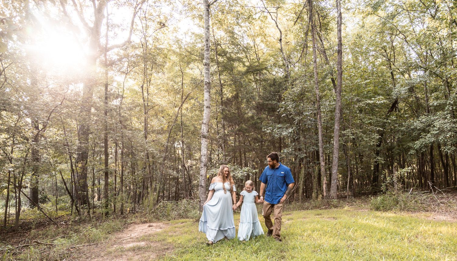 A group walks together on a sunlit wooded path during golden hour, with trees creating a natural backdrop.