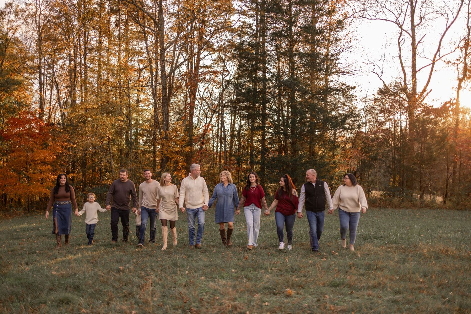 Extended family group walking together through autumn forest at sunset wearing coordinated neutral colors.