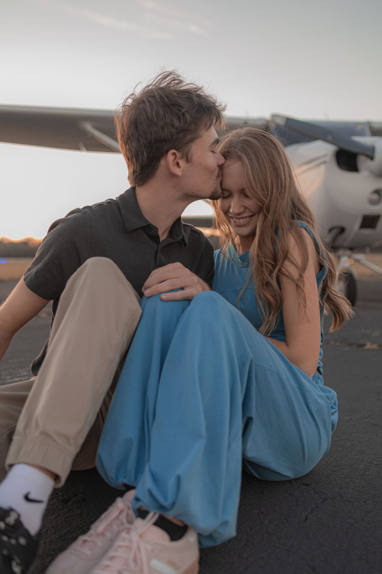 A romantic moment unfolds between a couple on an airport tarmac during golden hour.