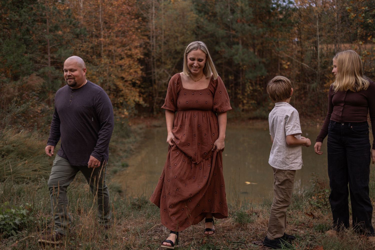 Family walking together through a wooded area during golden hour with fall foliage in the background.