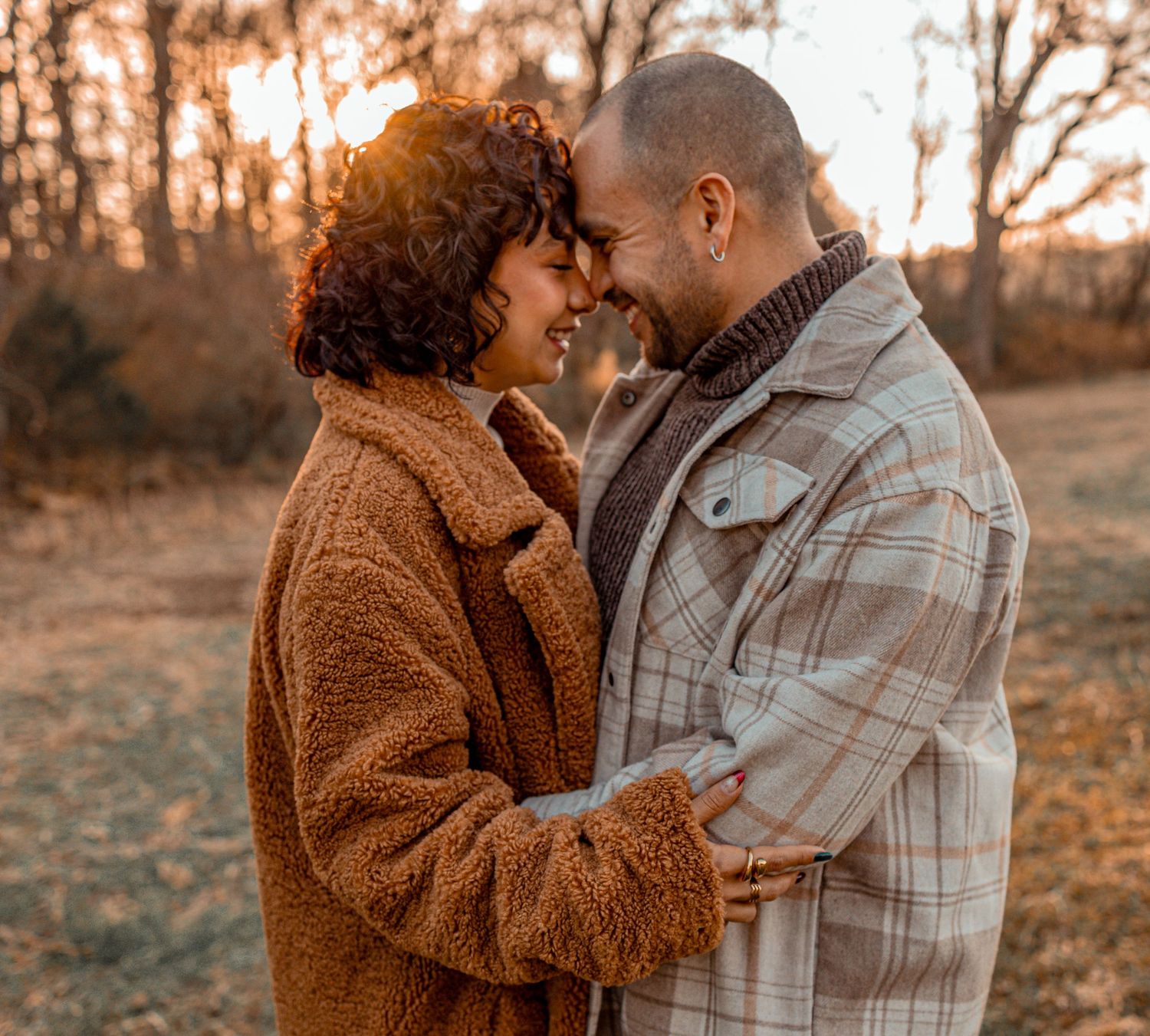 A couple embraces in a warm golden sunset light while wearing cozy fall clothing in an outdoor setting.