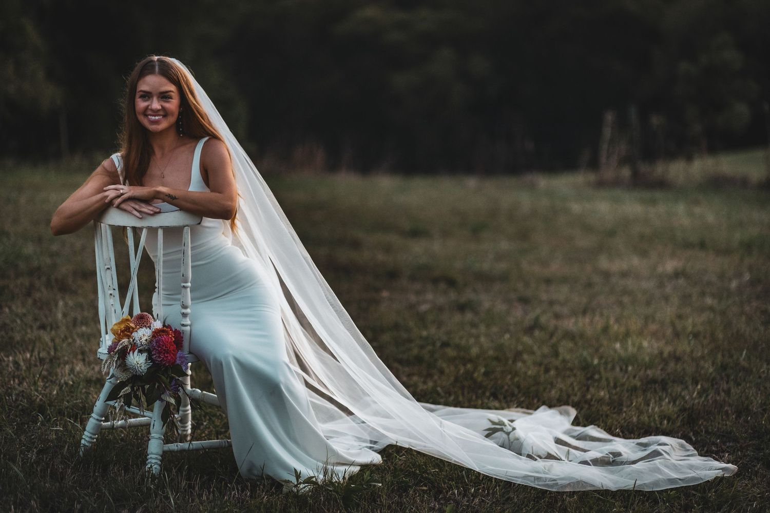 A person in a flowing white wedding dress stands in a rustic outdoor setting at golden hour.