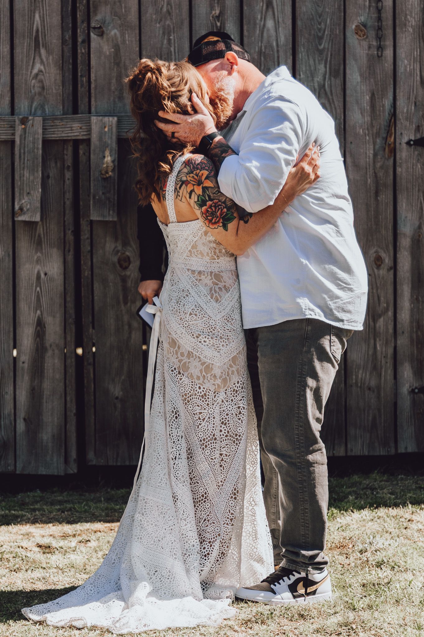 A romantic wedding kiss in front of a rustic wooden barn wall with the bride wearing a delicate lace gown.