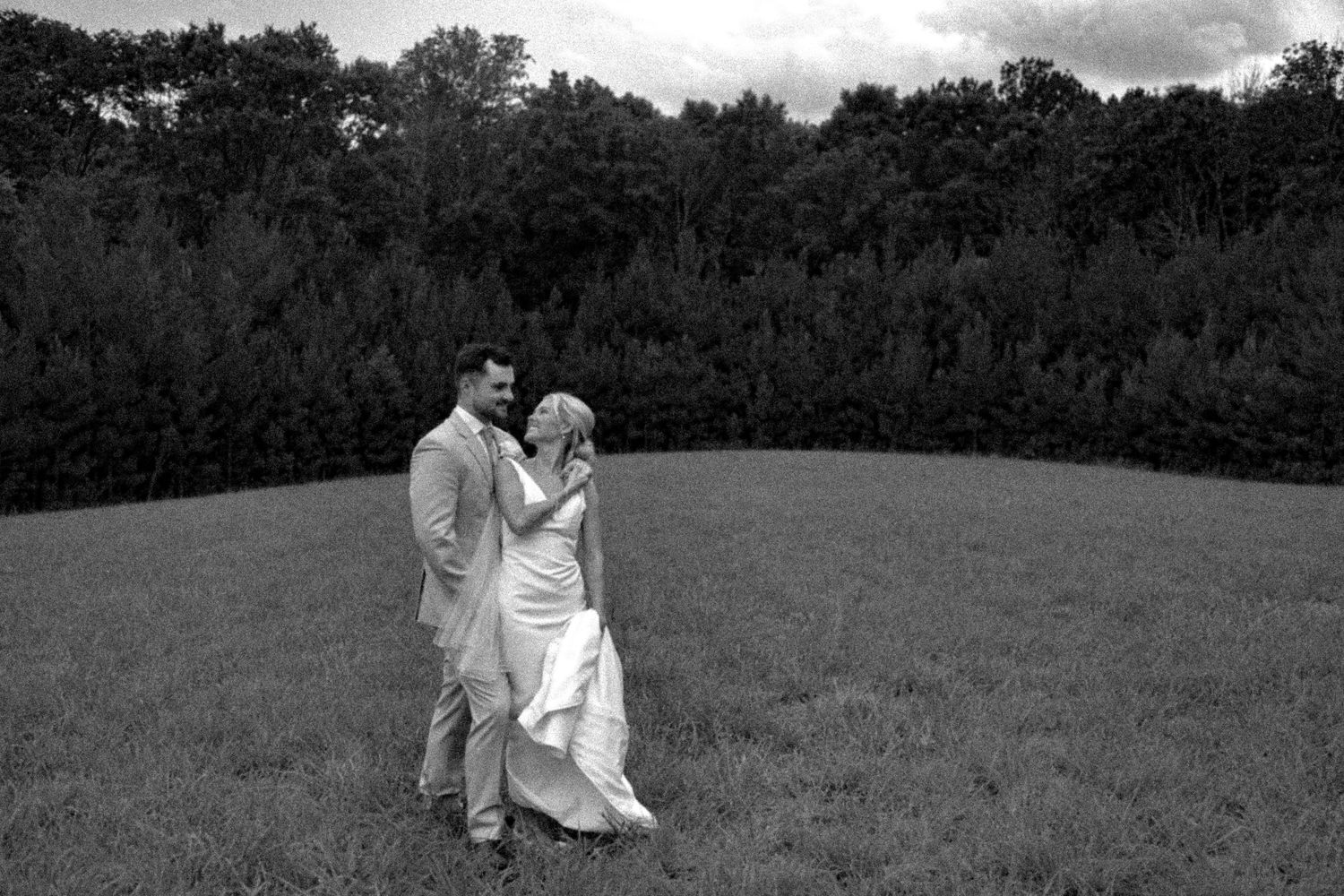 A black and white portrait of newlyweds sharing an intimate moment in a meadow.