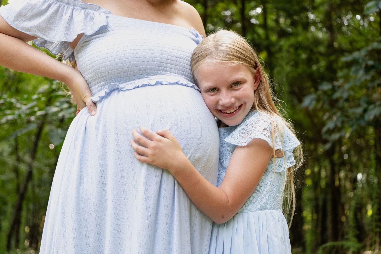 A sweet candid moment between two children in light blue dresses as they embrace outdoors in a garden setting.