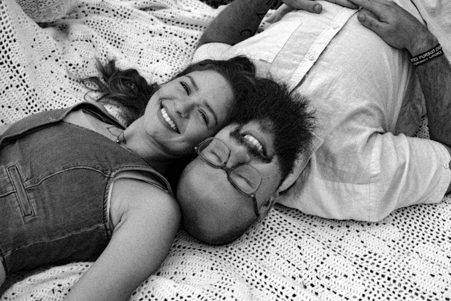 Two people lying on a white lace blanket sharing a joyful moment in black and white.