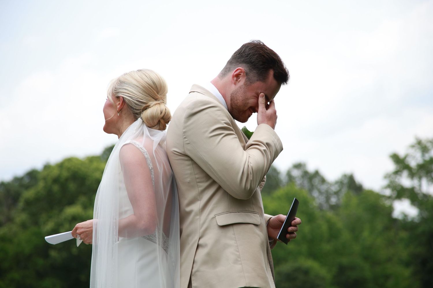 Couple sharing emotional moment during outdoor wedding ceremony while holding papers.