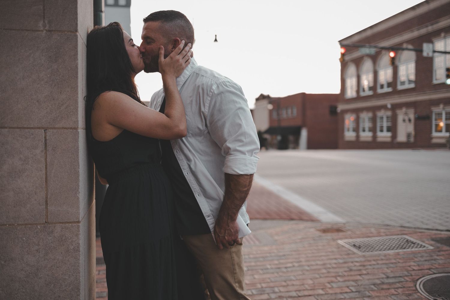 Couple sharing intimate moment against brick wall in urban setting.