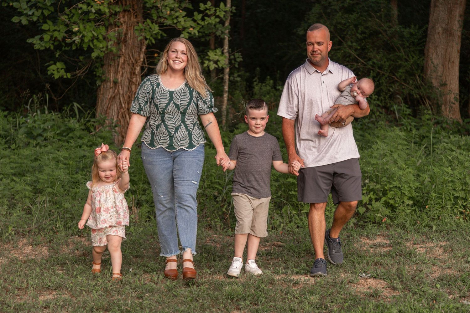 Family enjoying a summer walk together through a wooded path in matching neutral colored outfits.