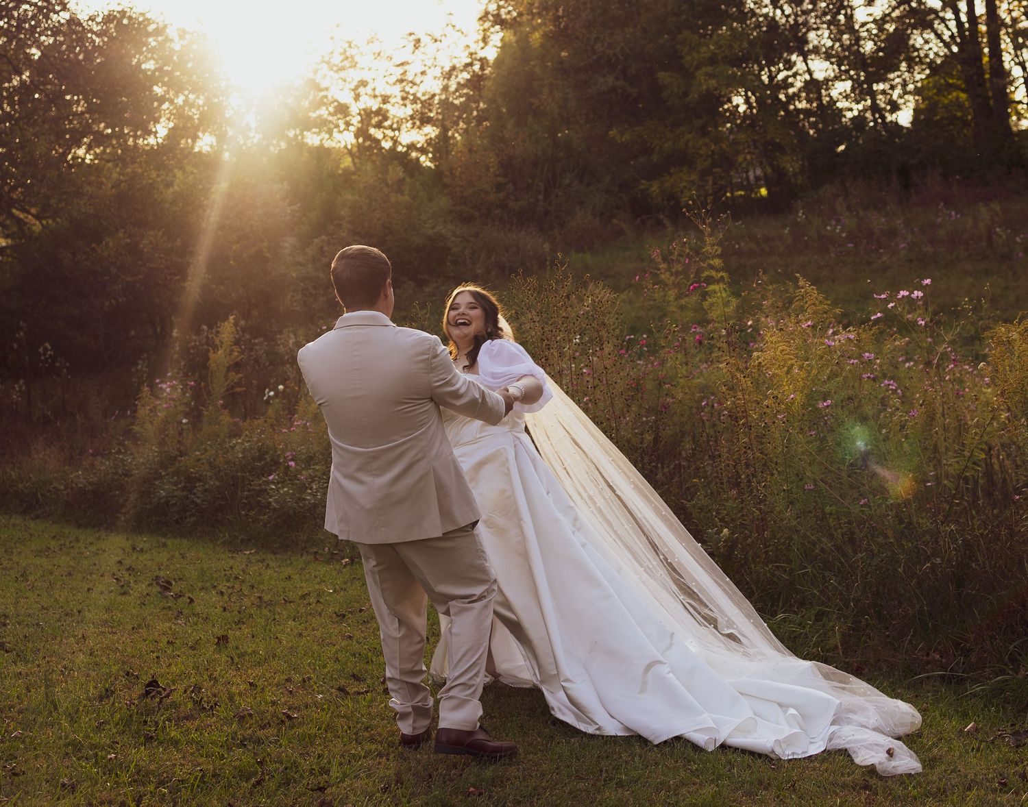 A couple in wedding attire poses in a golden sunlit field during sunset for romantic outdoor portraits.