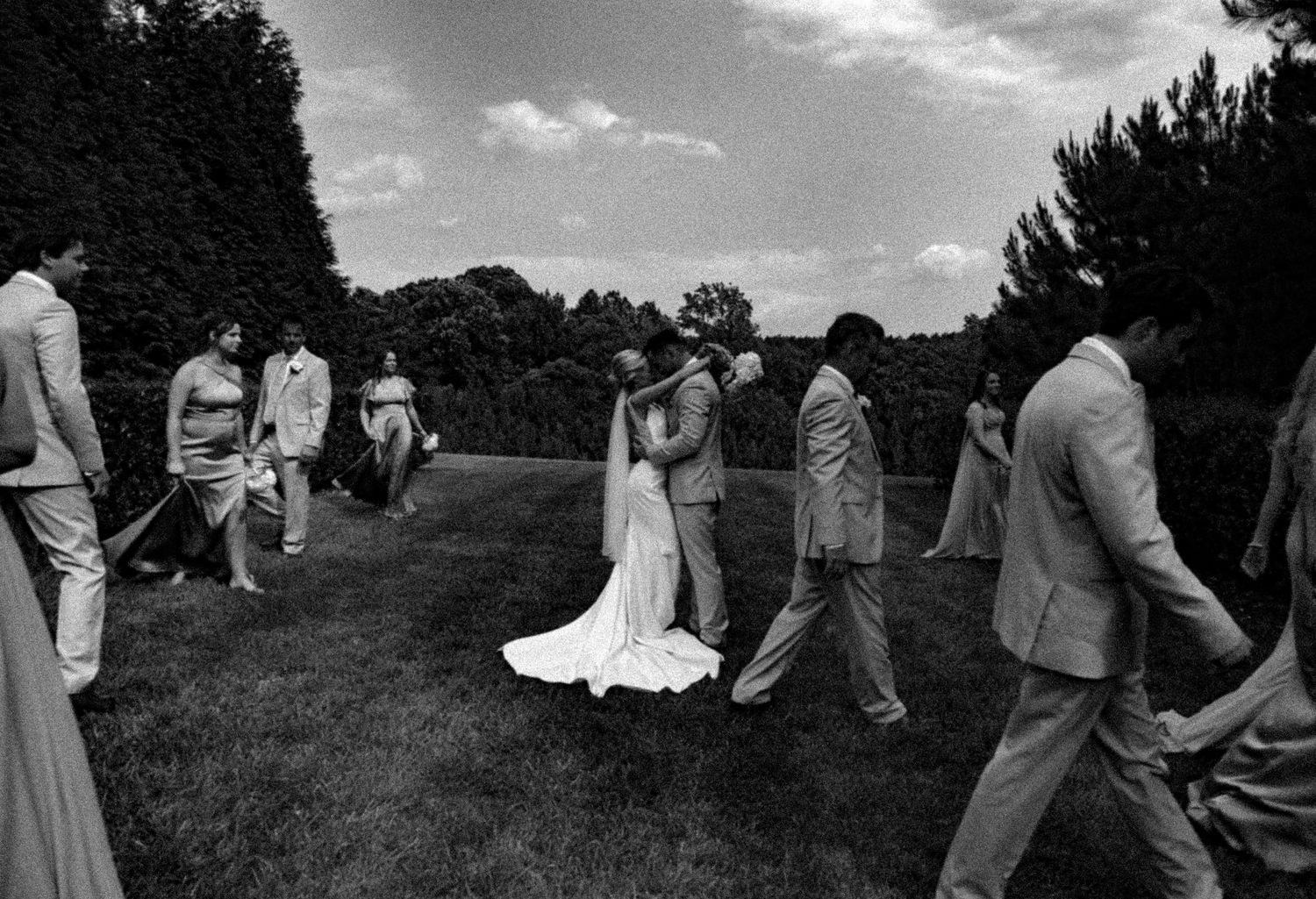 Black and white wedding party processional walking across field.