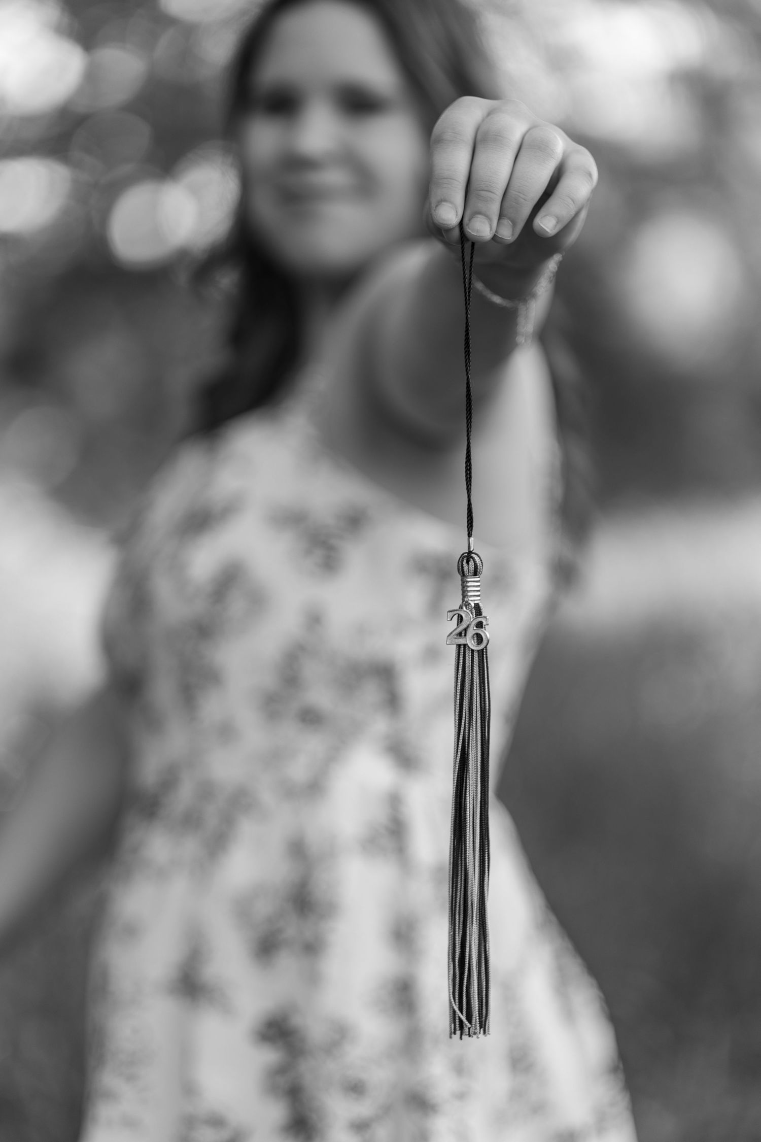 Black and white photo of a smiling woman holding a graduation tassel outdoors.