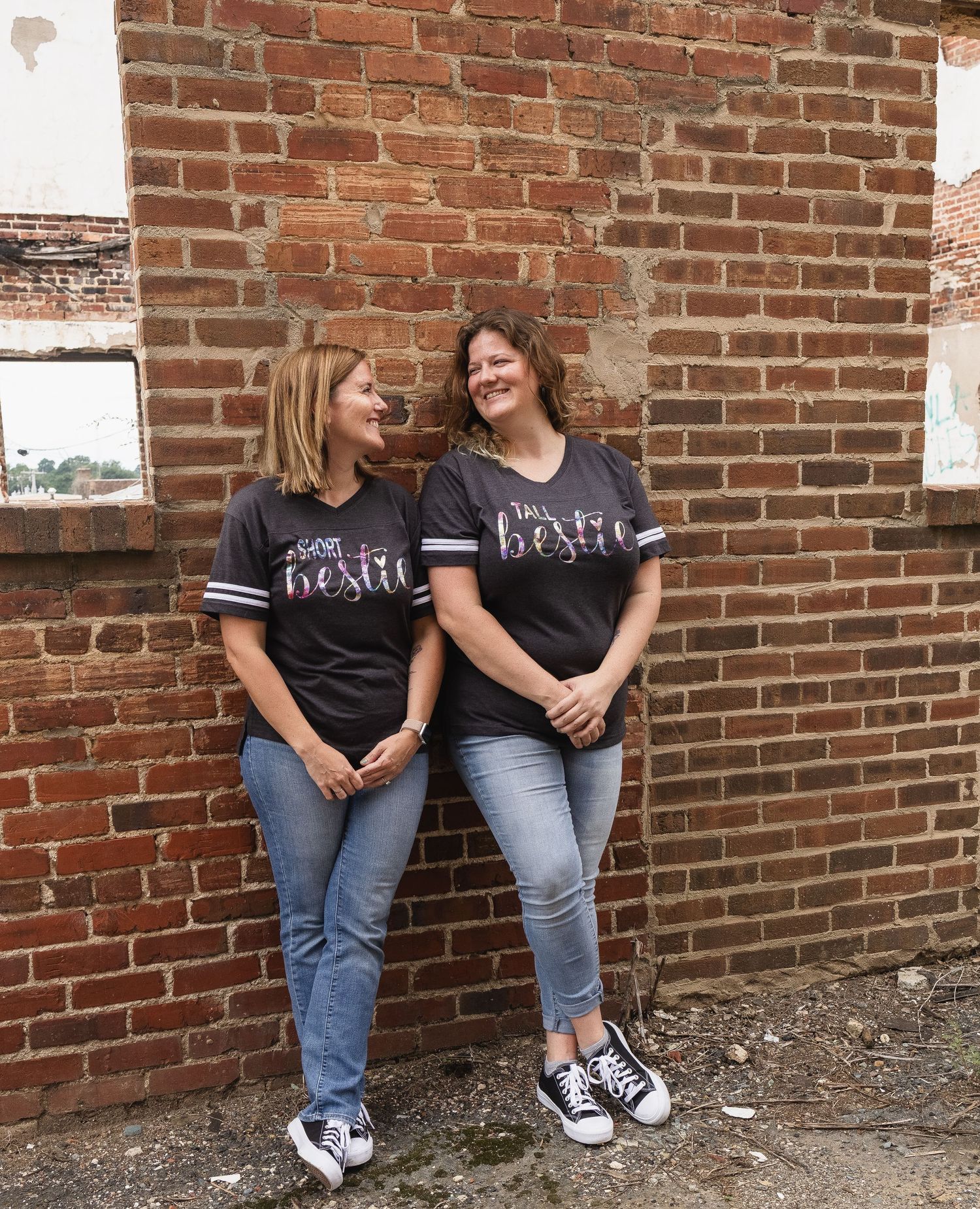 Two people in black t-shirts and jeans lean against a brick wall in three casual portrait poses.