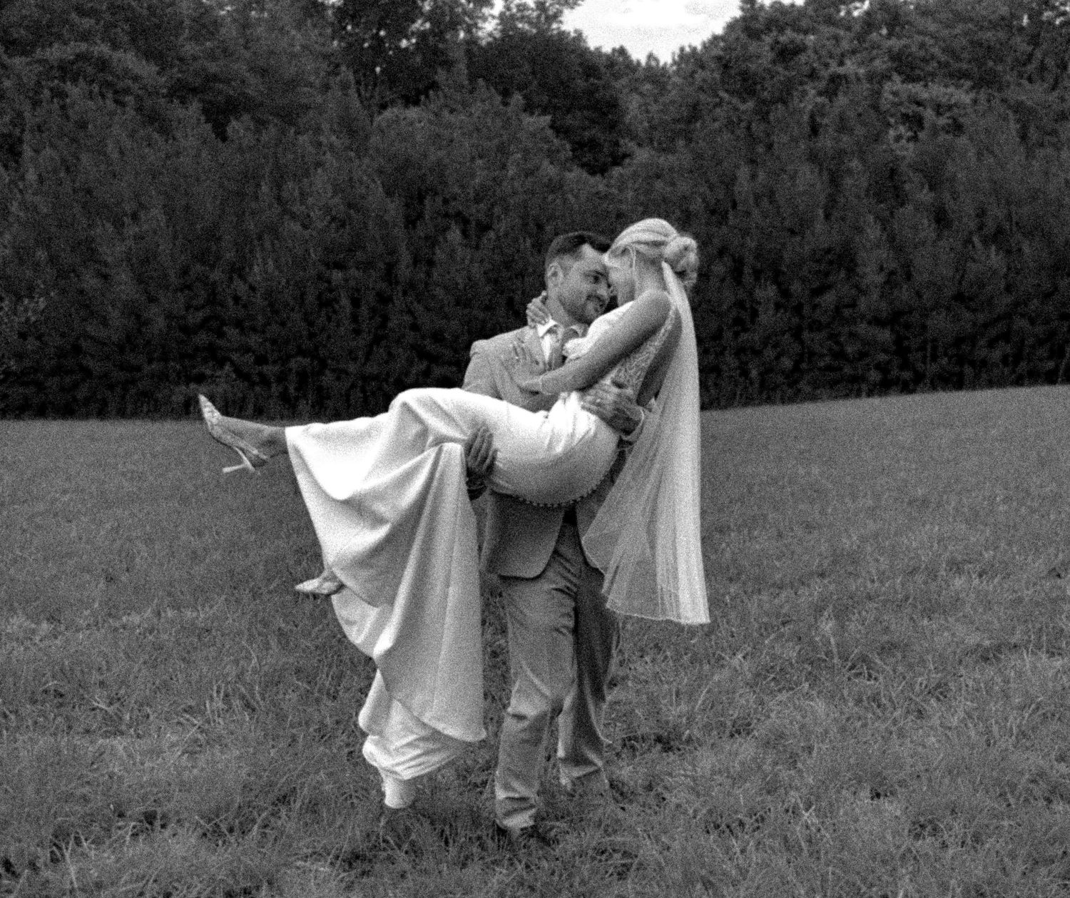 A playful black and white wedding photo showing a romantic lift pose in an outdoor setting.
